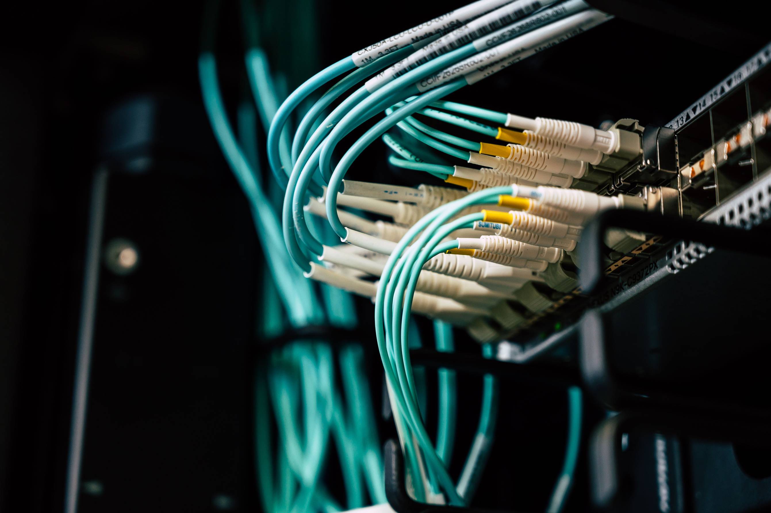 Wide view of a server room aisle with racks and cabling, network cables plugged into a server rack in a data center